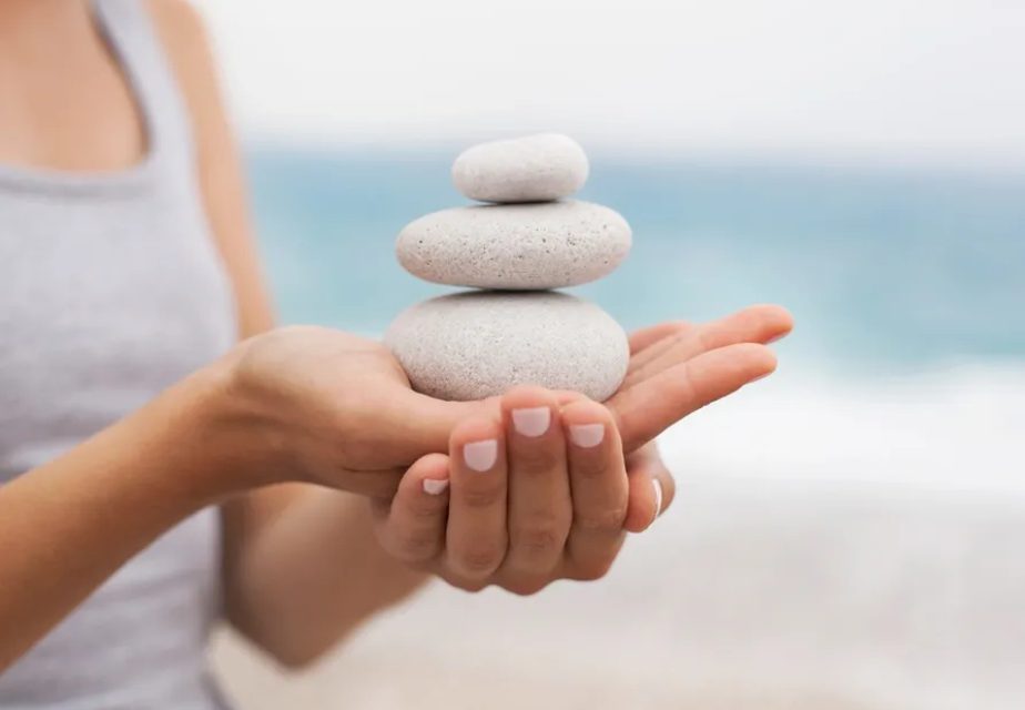 Hands holding stacked stones by beach.