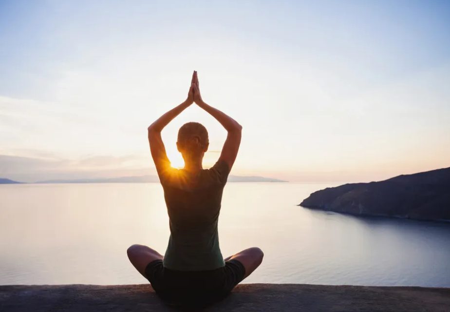 Person meditating by the ocean at sunset.