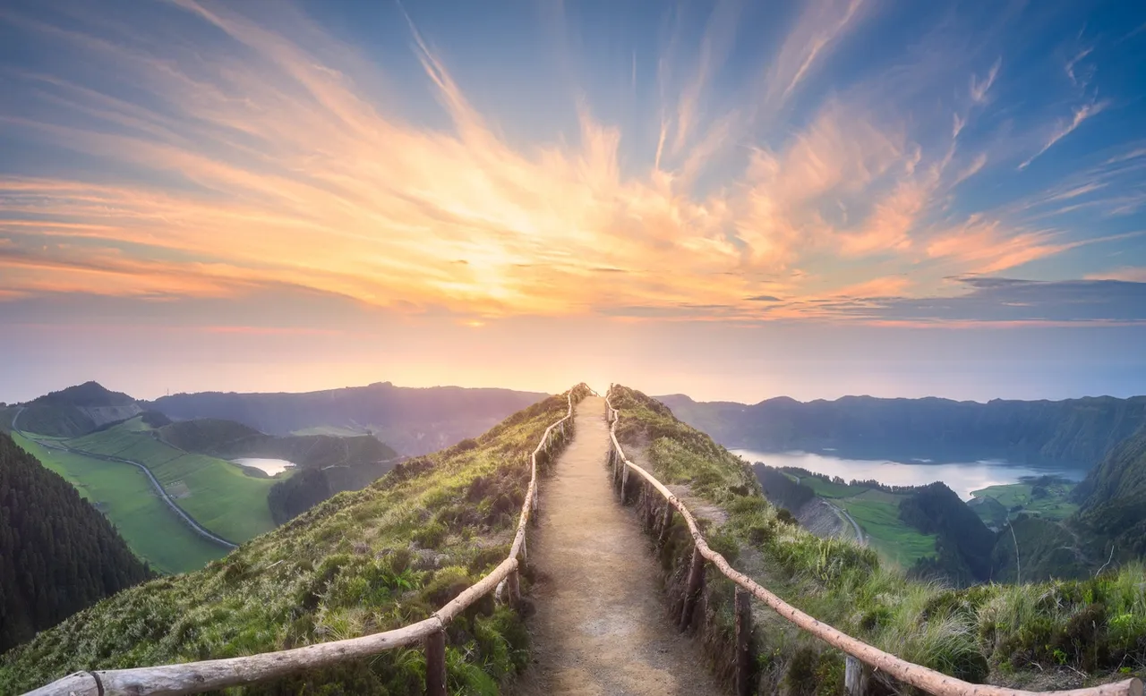 Sunset over a winding mountain path with railing.