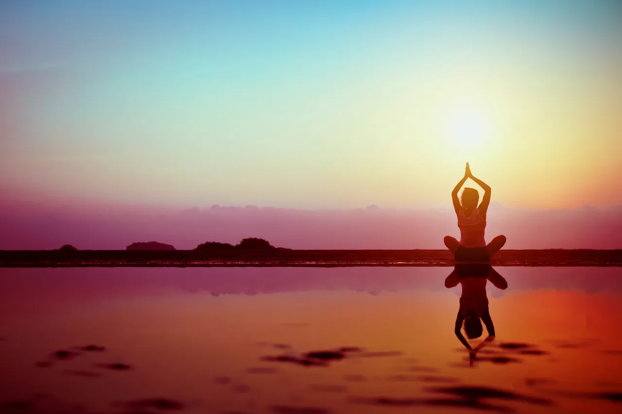Person practicing yoga during sunset by the water.