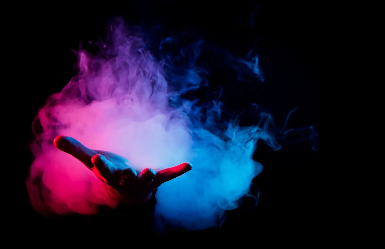Hand forming a rock gesture surrounded by colorful smoke.