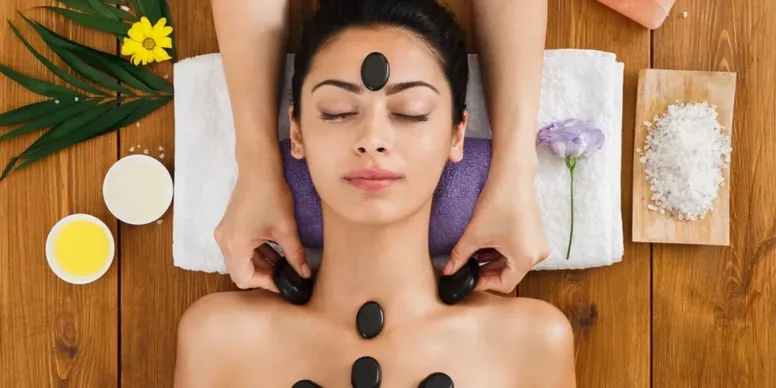 Woman receiving a hot stone massage with stones on her forehead and chest.