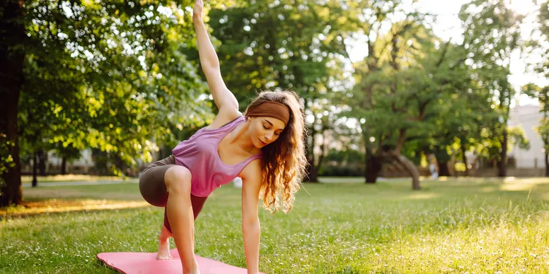 Woman practicing yoga outdoors in a park, stretching with focus.