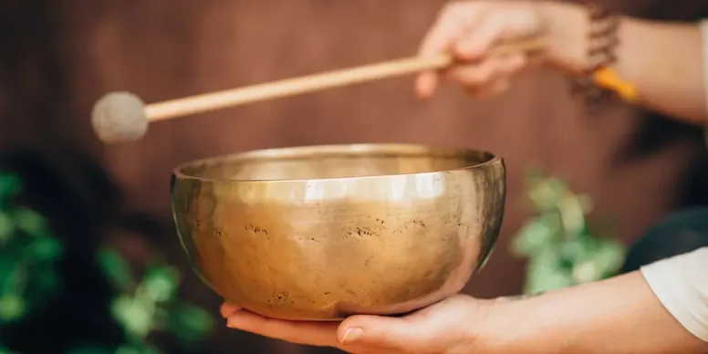 A person playing a brass singing bowl with a wooden mallet.