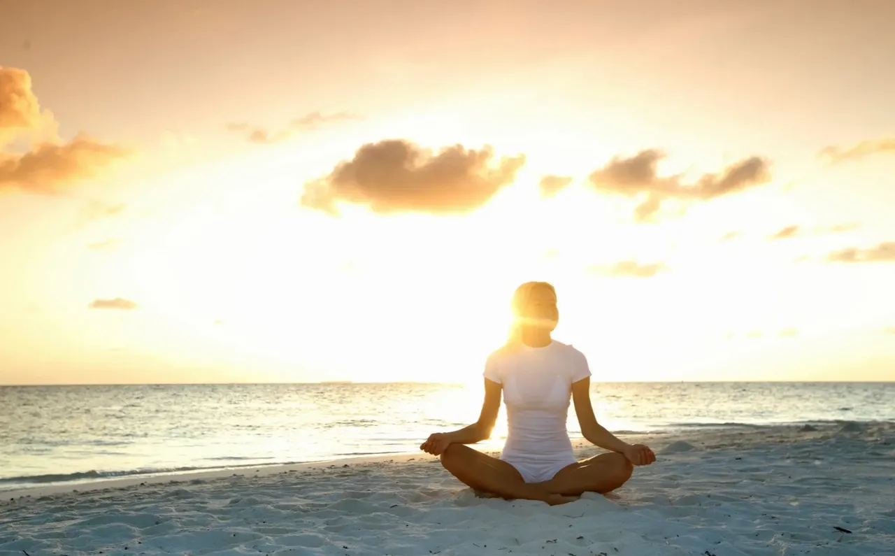 Person meditating by the ocean at sunset.