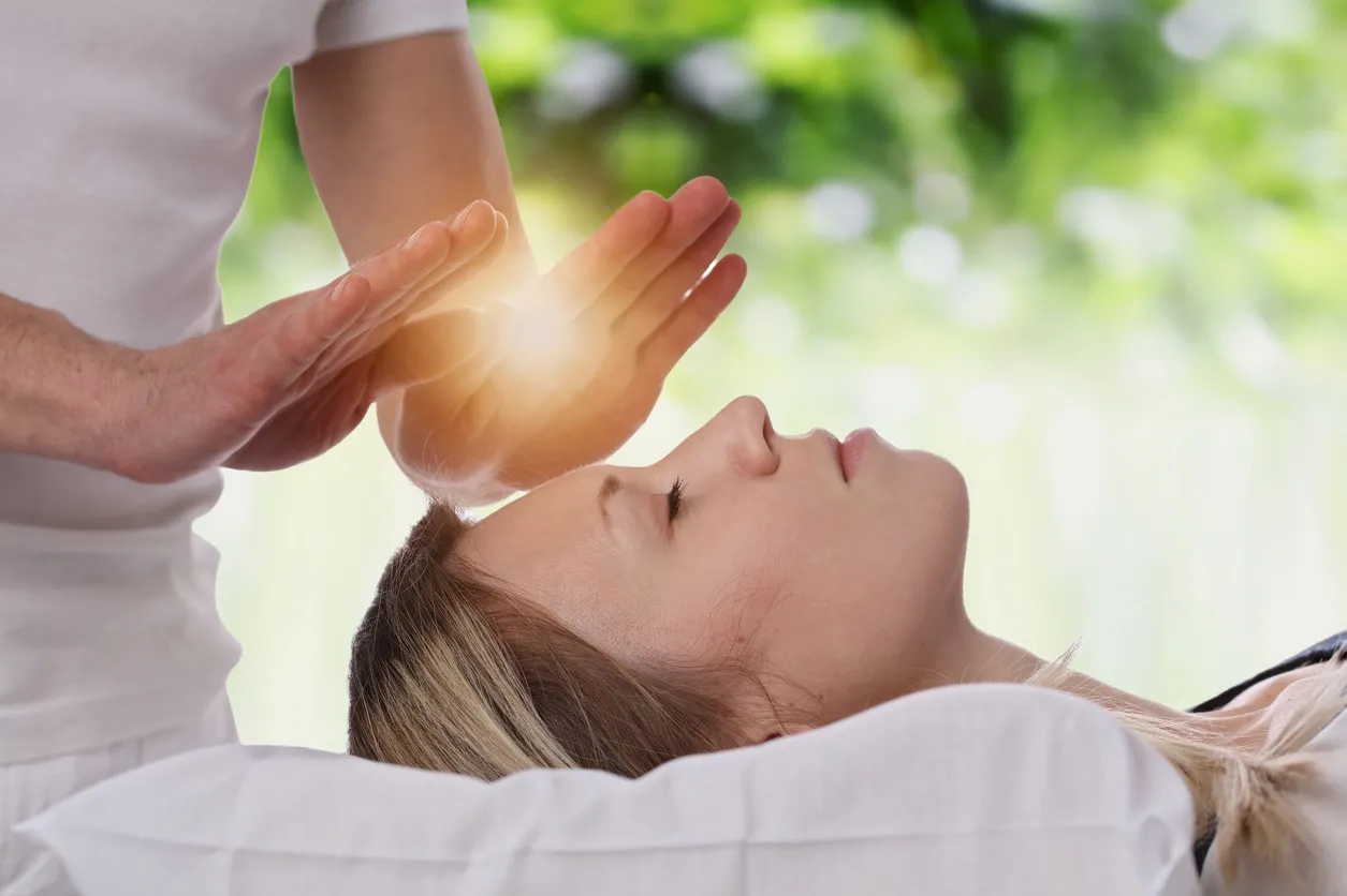 A person receiving energy healing with hands glowing above their forehead.