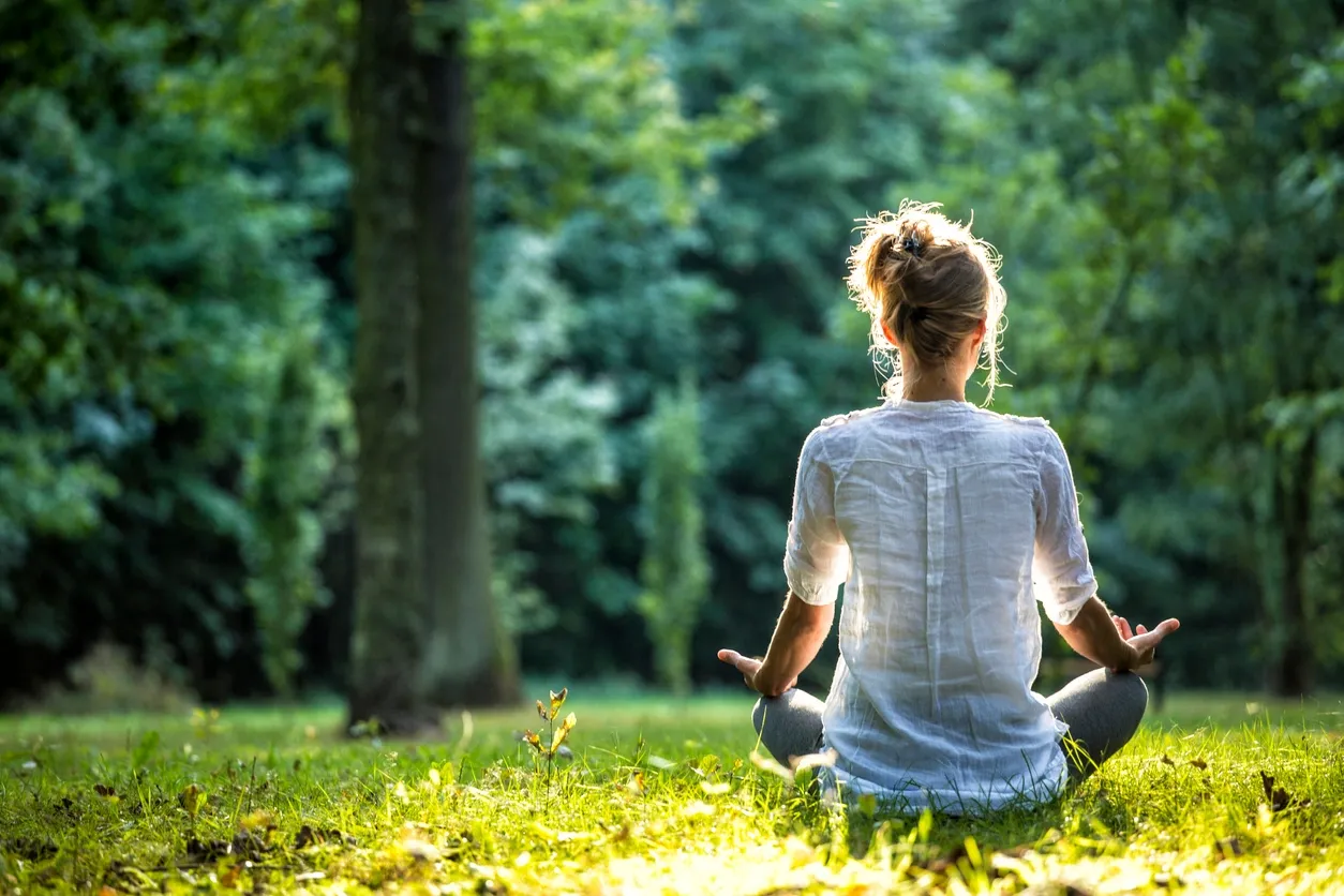 Person meditating outdoors in a peaceful green park.