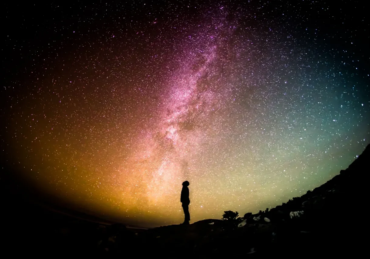Silhouette of a person under the colorful Milky Way galaxy.