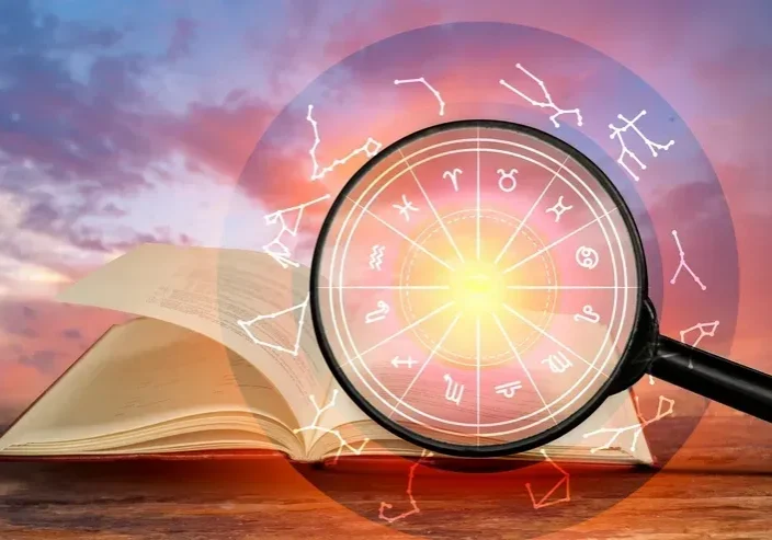 Magnifying glass highlighting zodiac signs over an open book with a mystical background.