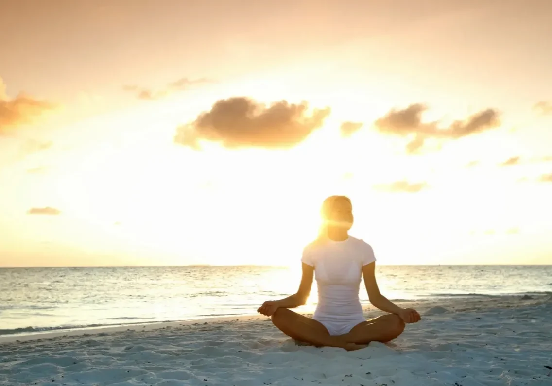Person meditating by the ocean at sunset.