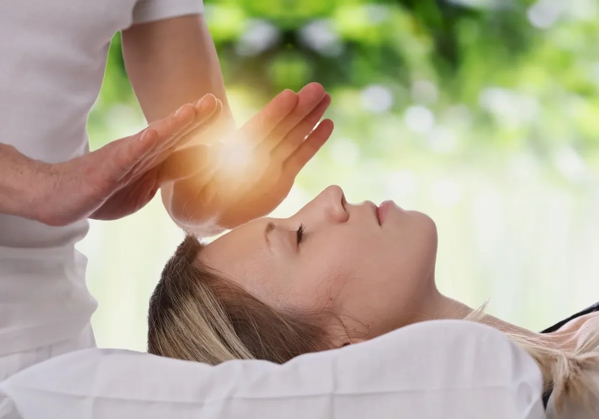 A person receiving energy healing with hands glowing above their forehead.