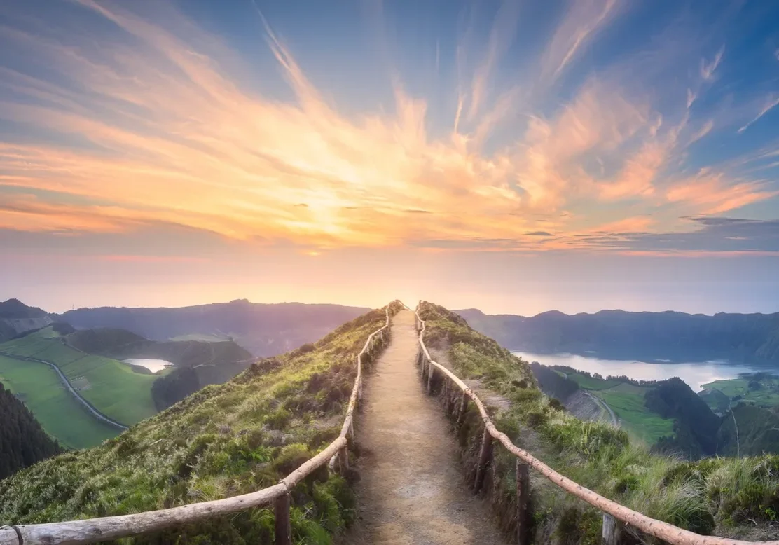 Sunset over a winding mountain path with railing.