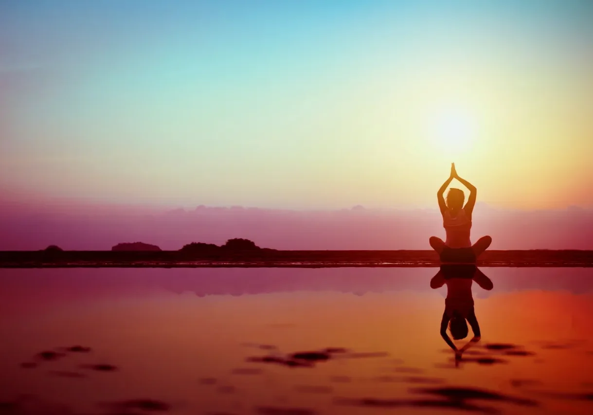 Person practicing yoga during sunset by the water.