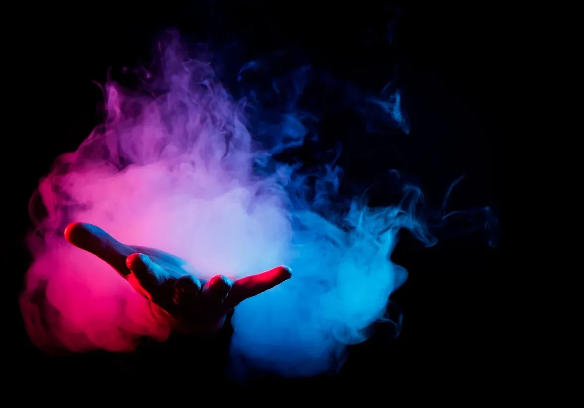 Hand forming a rock gesture surrounded by colorful smoke.
