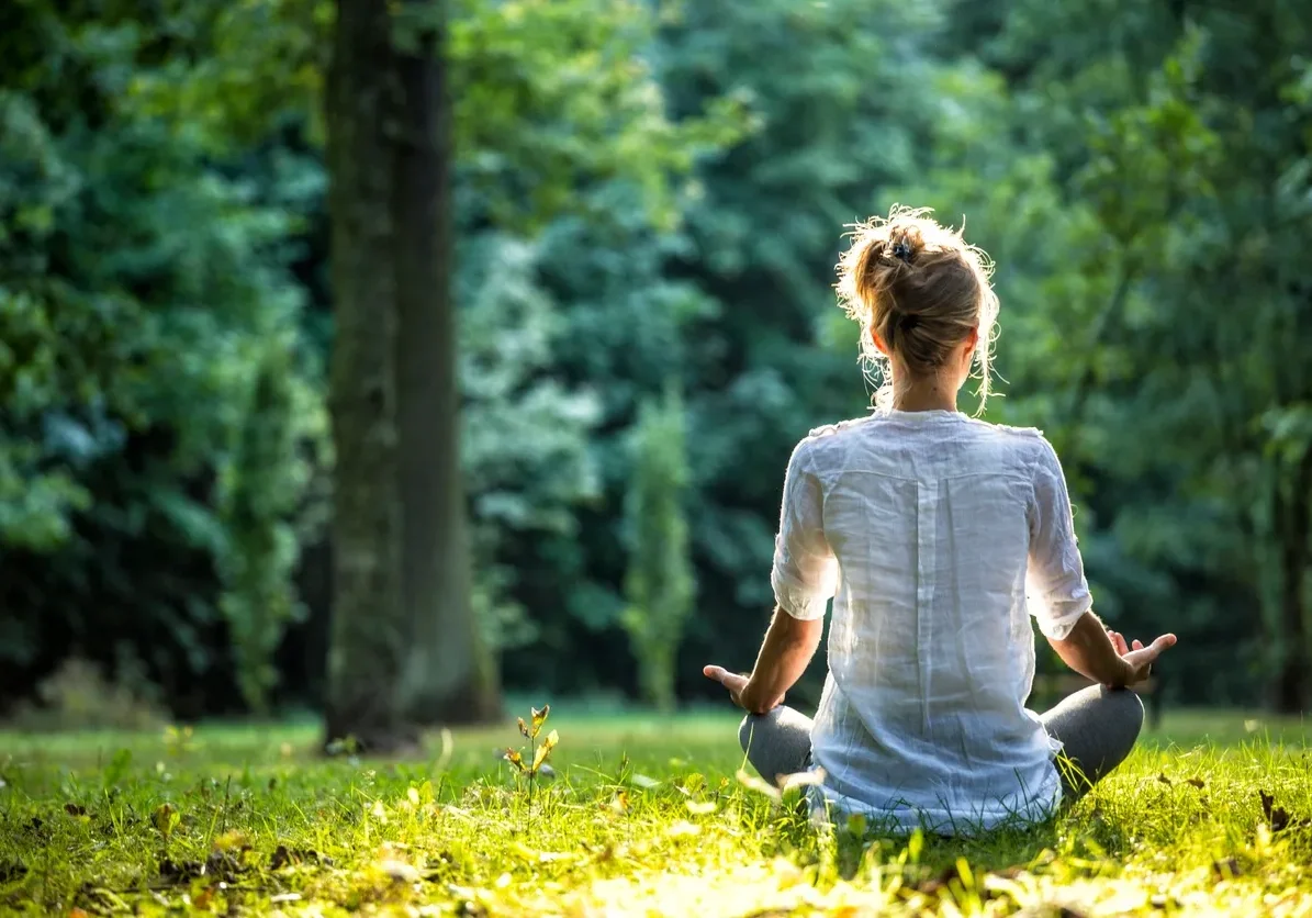 Person meditating outdoors in a peaceful green park.